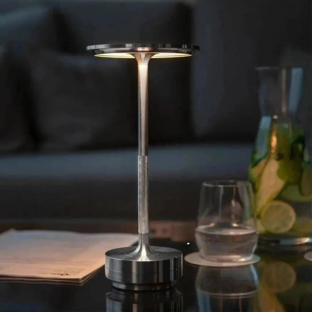 Luminária Halo Touch prateada acesa sobre mesa de apoio