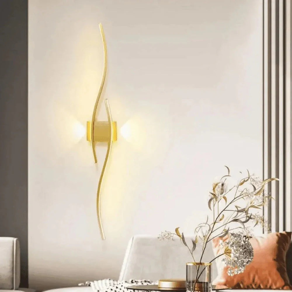 Arandela Linha Fluida dourada iluminando parede clara